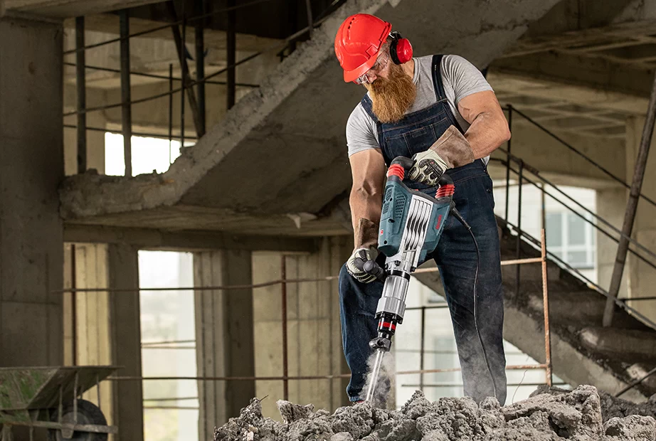 A construction worker is breaking concrete using a jackhammer